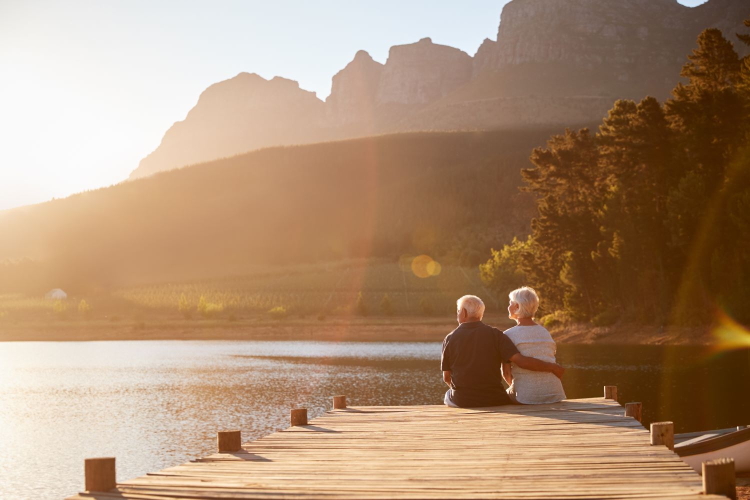 man and woman sitting on a dock on a lake surrounded by mountains on a bright sunny day roth 401k benefits kreitler financial wealth management